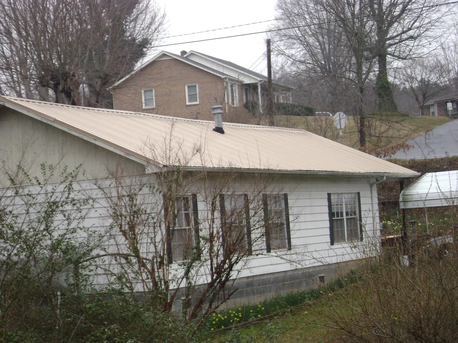 Tan metal roof on a white sided house set into a hillside — Commercial Roofing by Roofing Brothers in Payson